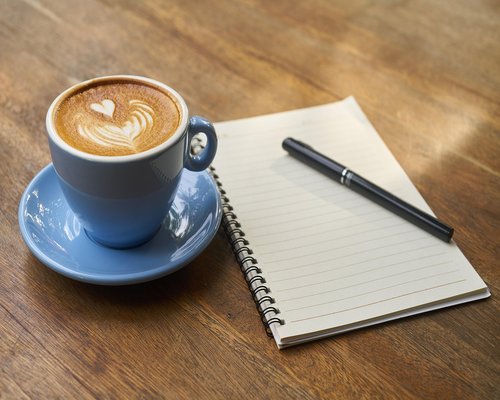 A cup of coffee next to a closed notebook on a desk